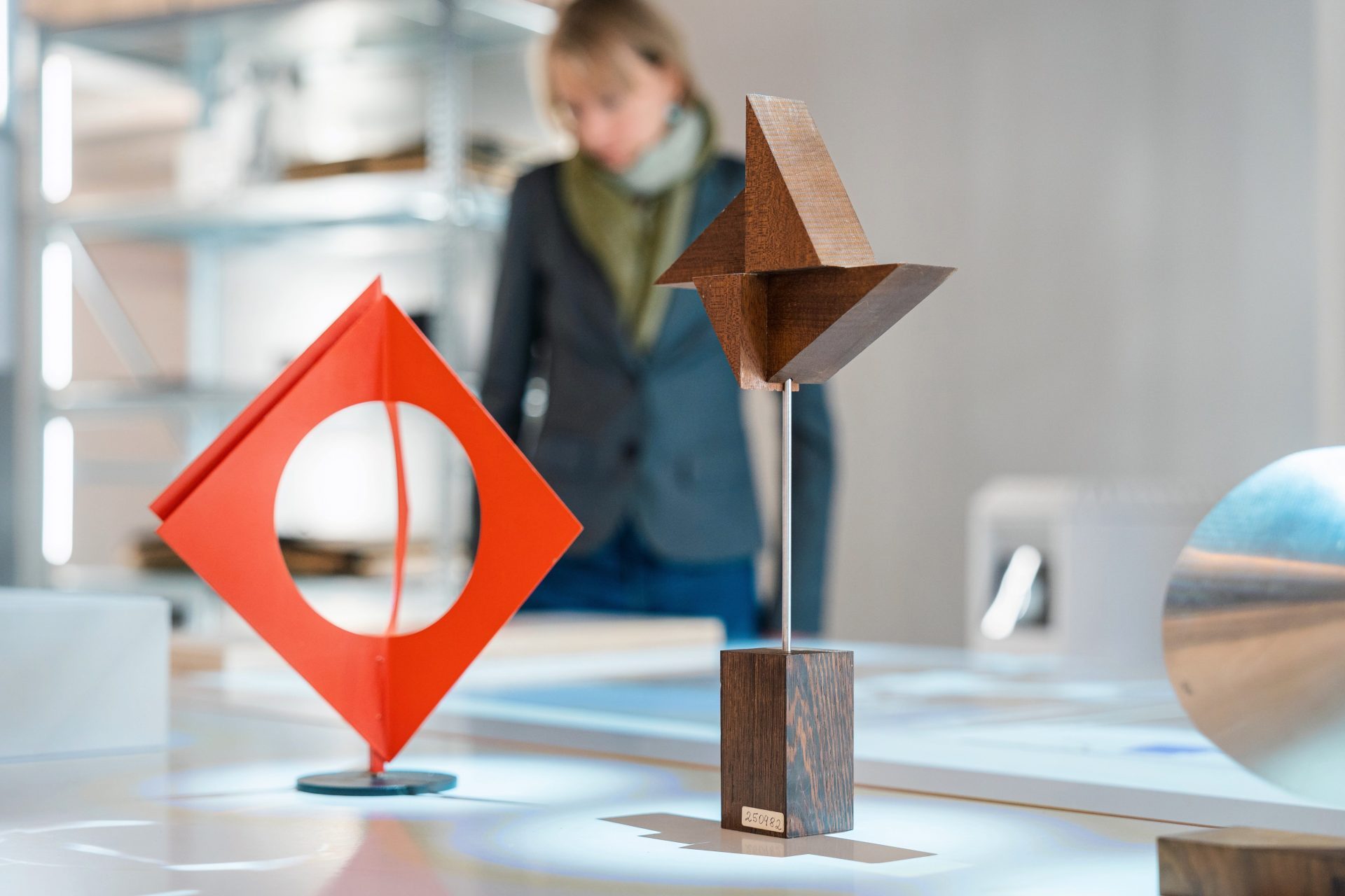 Abstract wooden and metal sculptures on a table, with a person in business attire in the background.