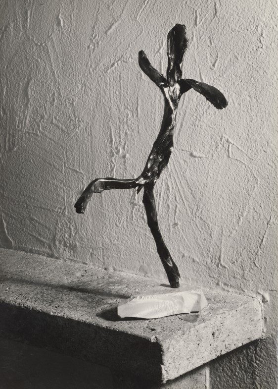 A black wire sculpture of a dancer on a stone surface, in front of a patterned wall.