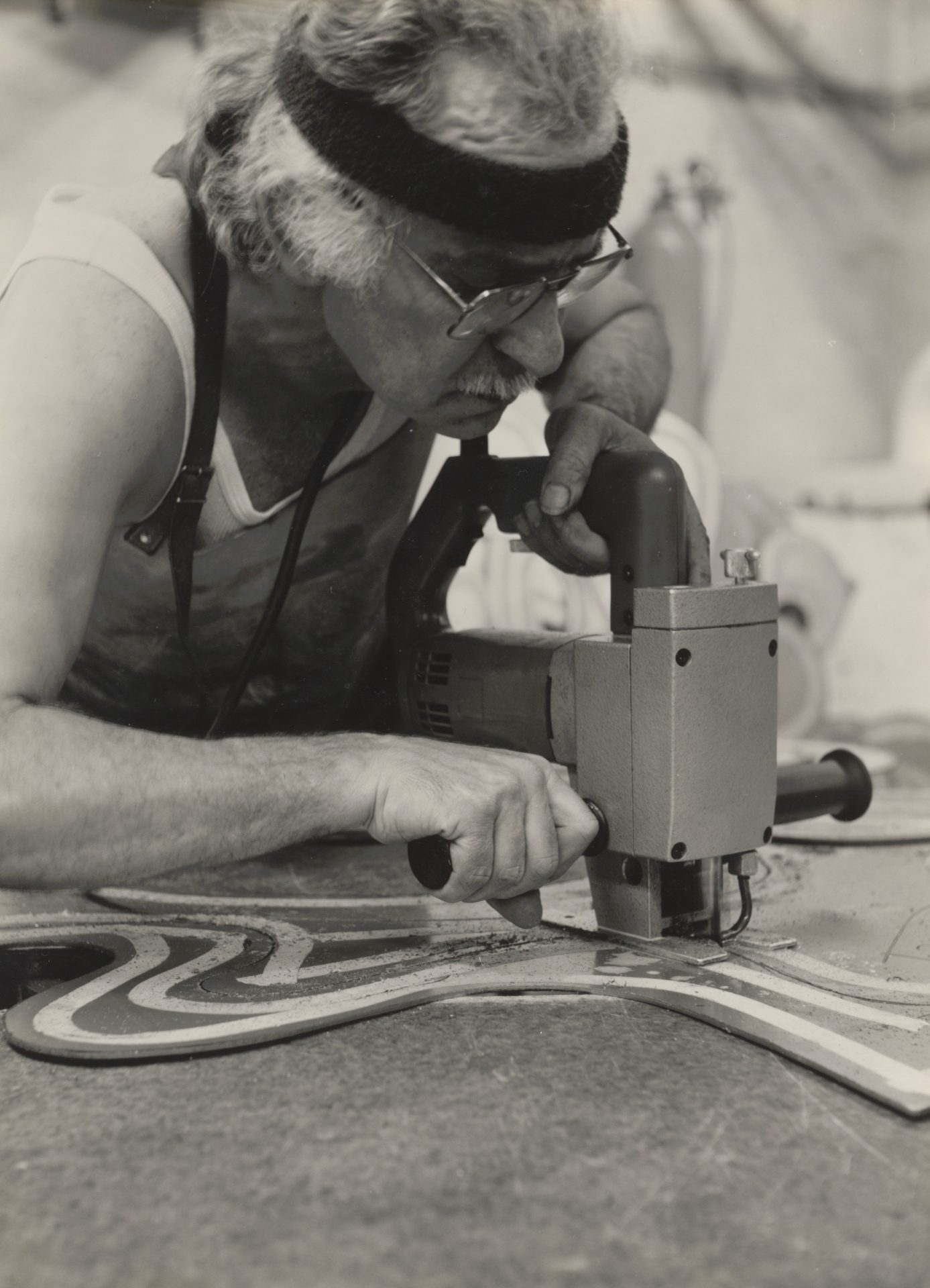 An older craftsman is using a jigsaw on a color sample on a wooden board.