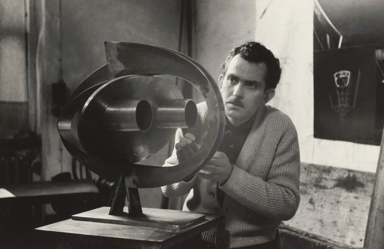 A man works intently on a metallic sculpture in a studio.