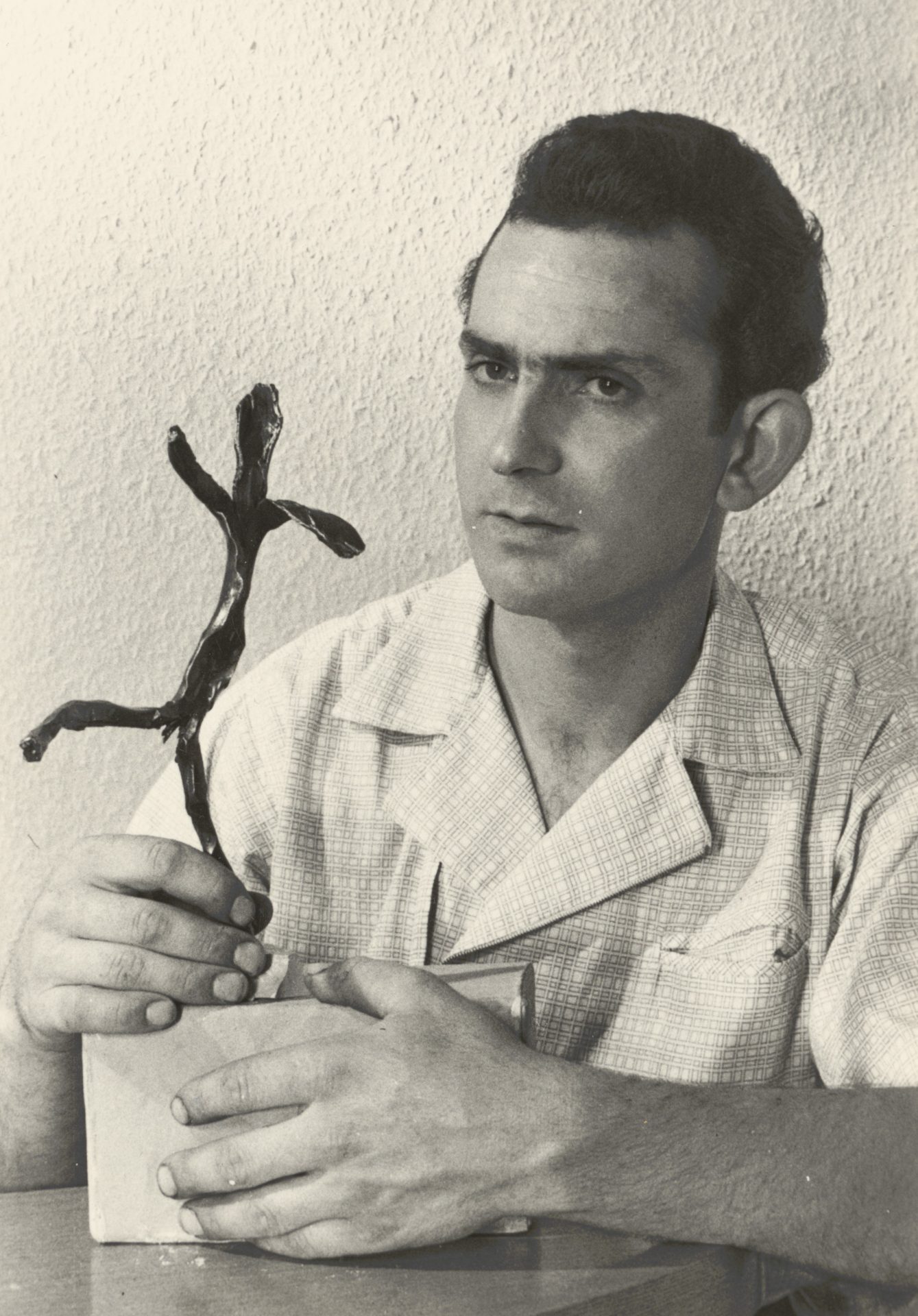 A man holds a metal art sculpture, looks thoughtful, and sits in front of a neutral wall.