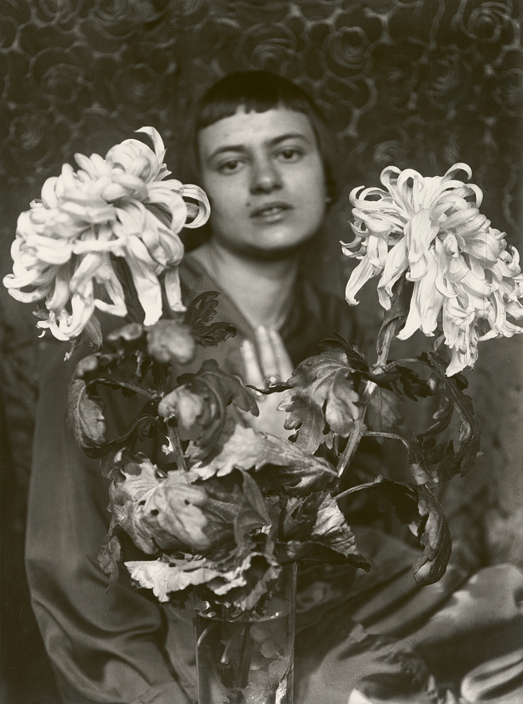 Porträt einer Frau hinter einem Strauß blühender Chrysanthemen, in Schwarz-Weiß mit verschwommenem Hintergrund.