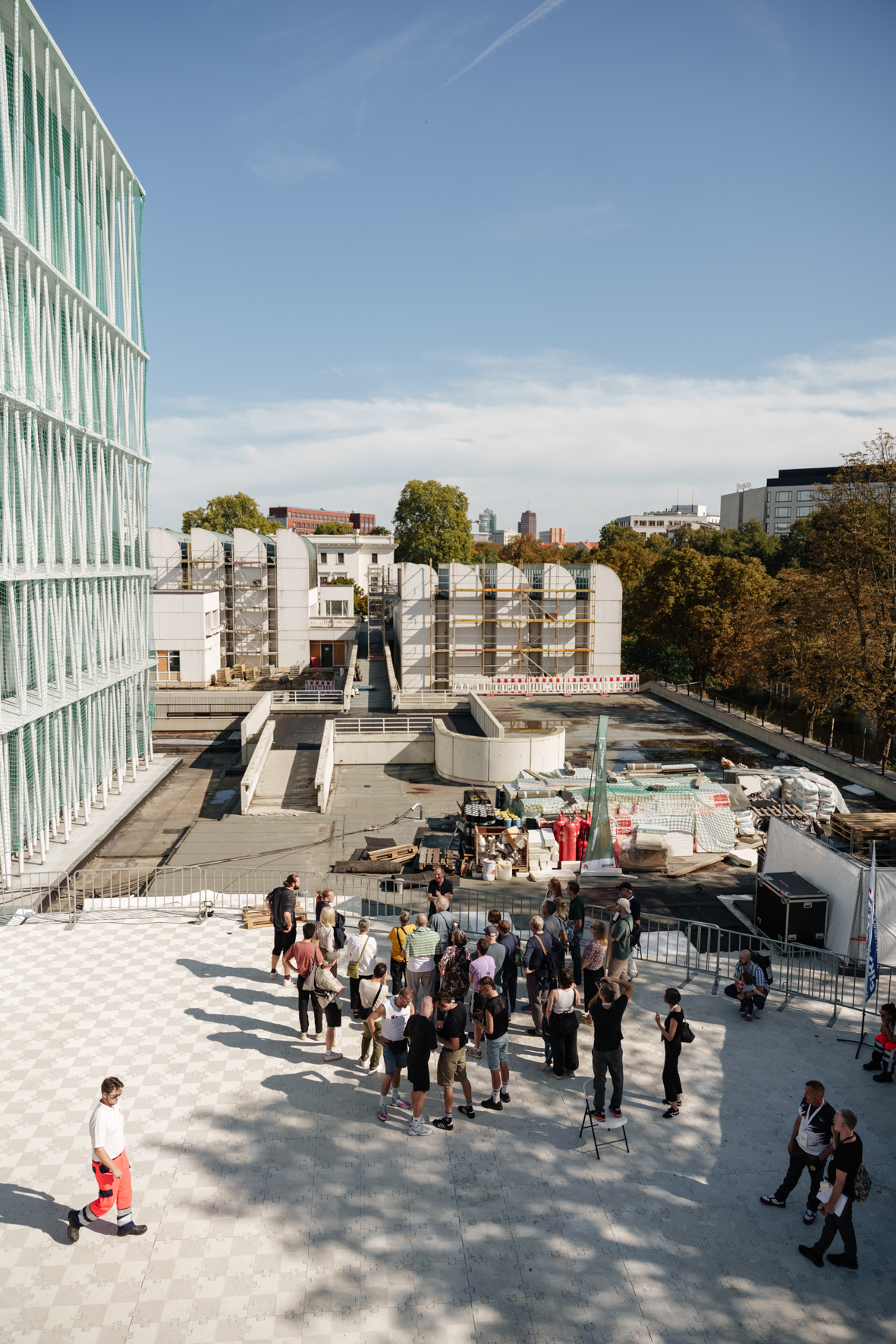Blick auf eine Gruppe von Menschen auf einer Baustelle mit moderner Architektur und wartenden Bauarbeiten im Hintergrund.