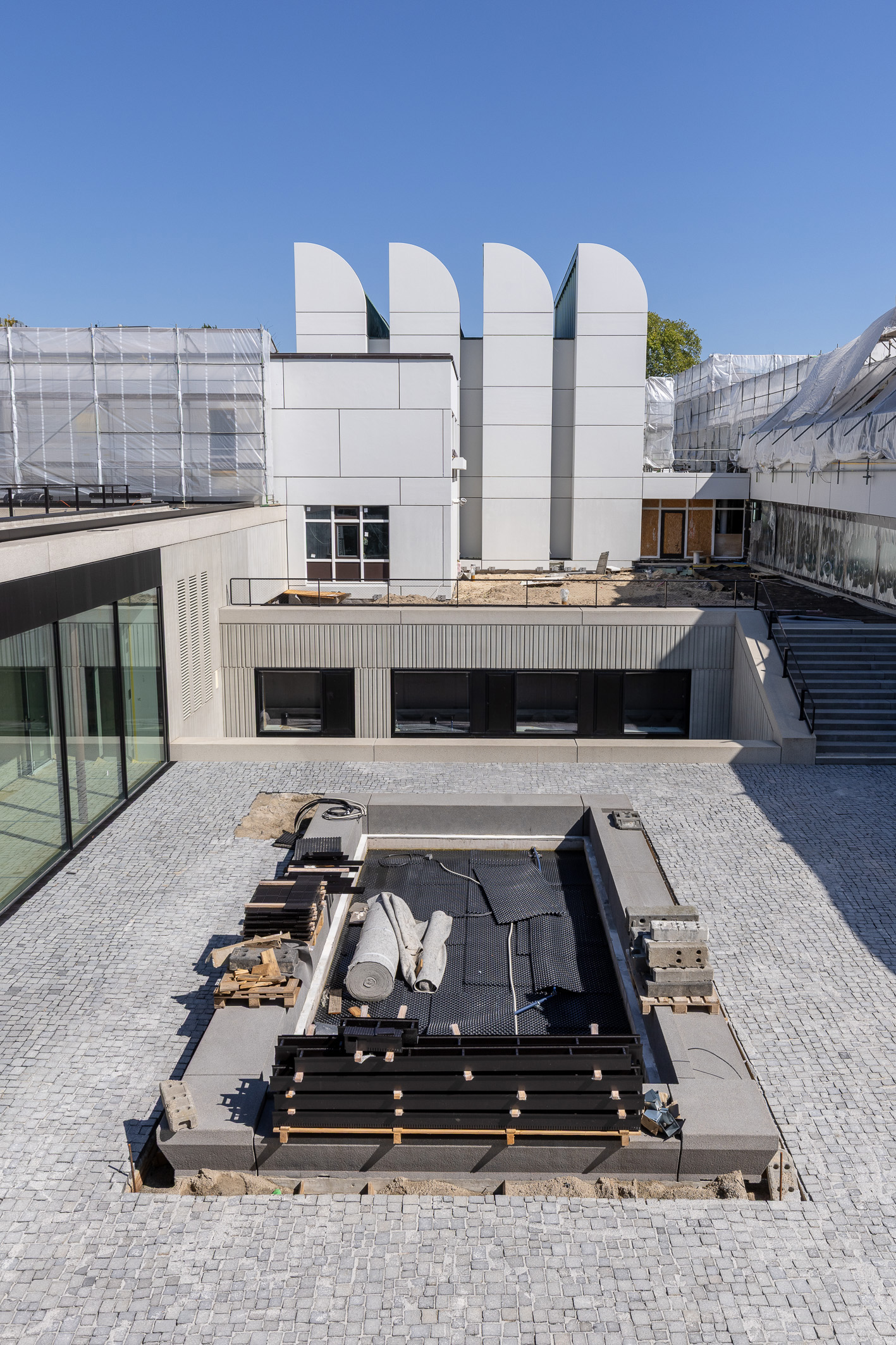 Bauarbeiten auf einer modernen Architektur mit Terrassenbereich, Steinen und Materialien im Freien. Klarer blauer Himmel.