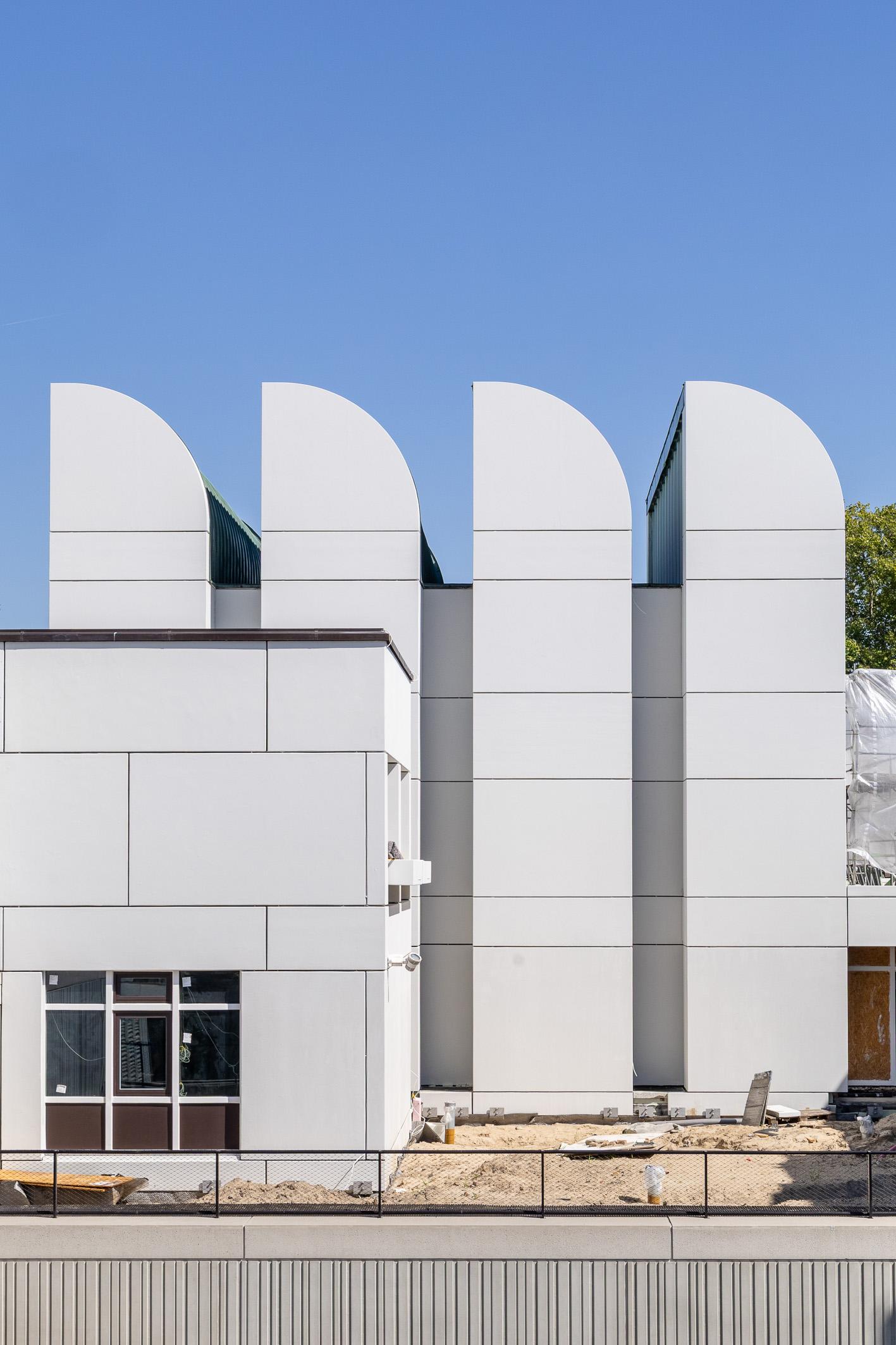 Moderne Architektur mit geschwungenen Dächern und weißen Fassaden vor blauem Himmel, teils noch im Bau.