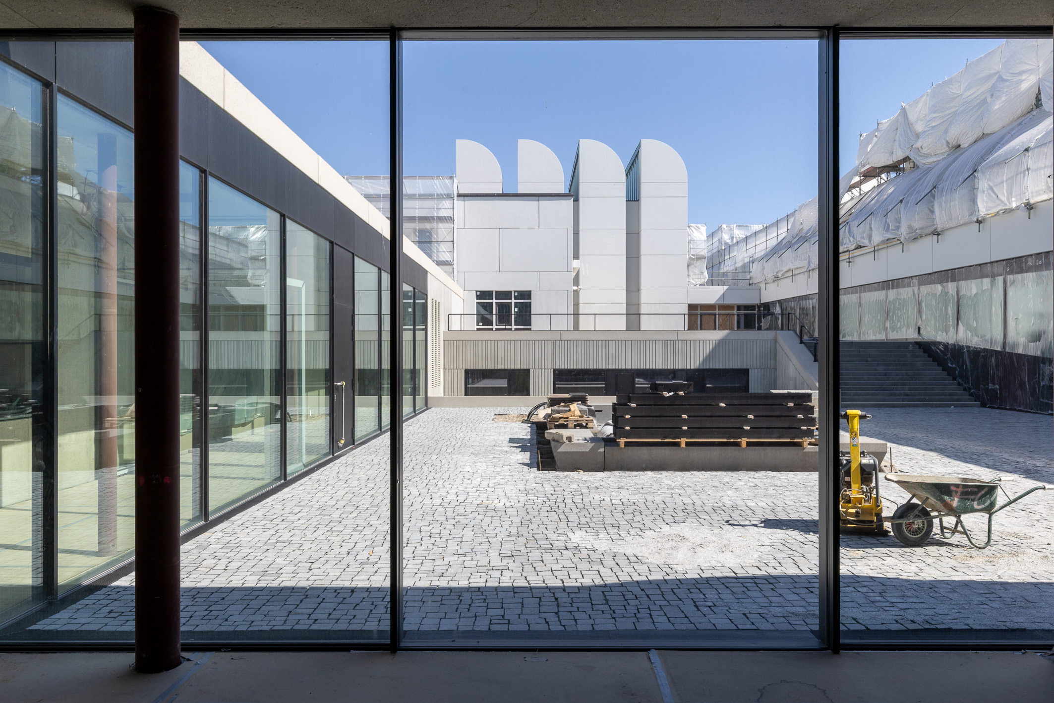 Moderne Architektur mit großen Fenstern, einem Innenhof aus Pflastersteinen und Baustellenmaterialien.