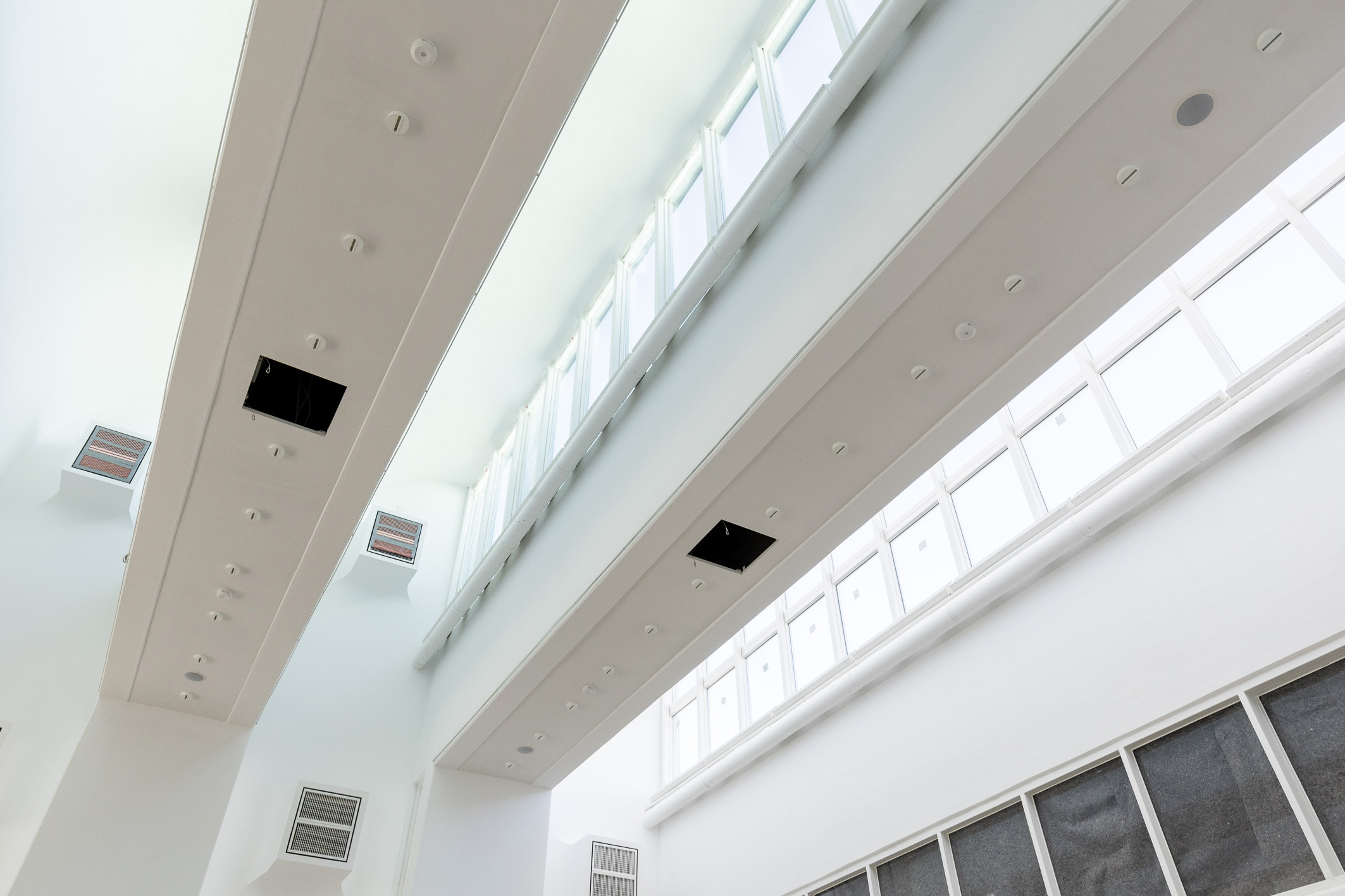Moderne Architekturszene mit hohen Decken, langen Lichtleisten und großen Fenstern, die viel Tageslicht einlassen.