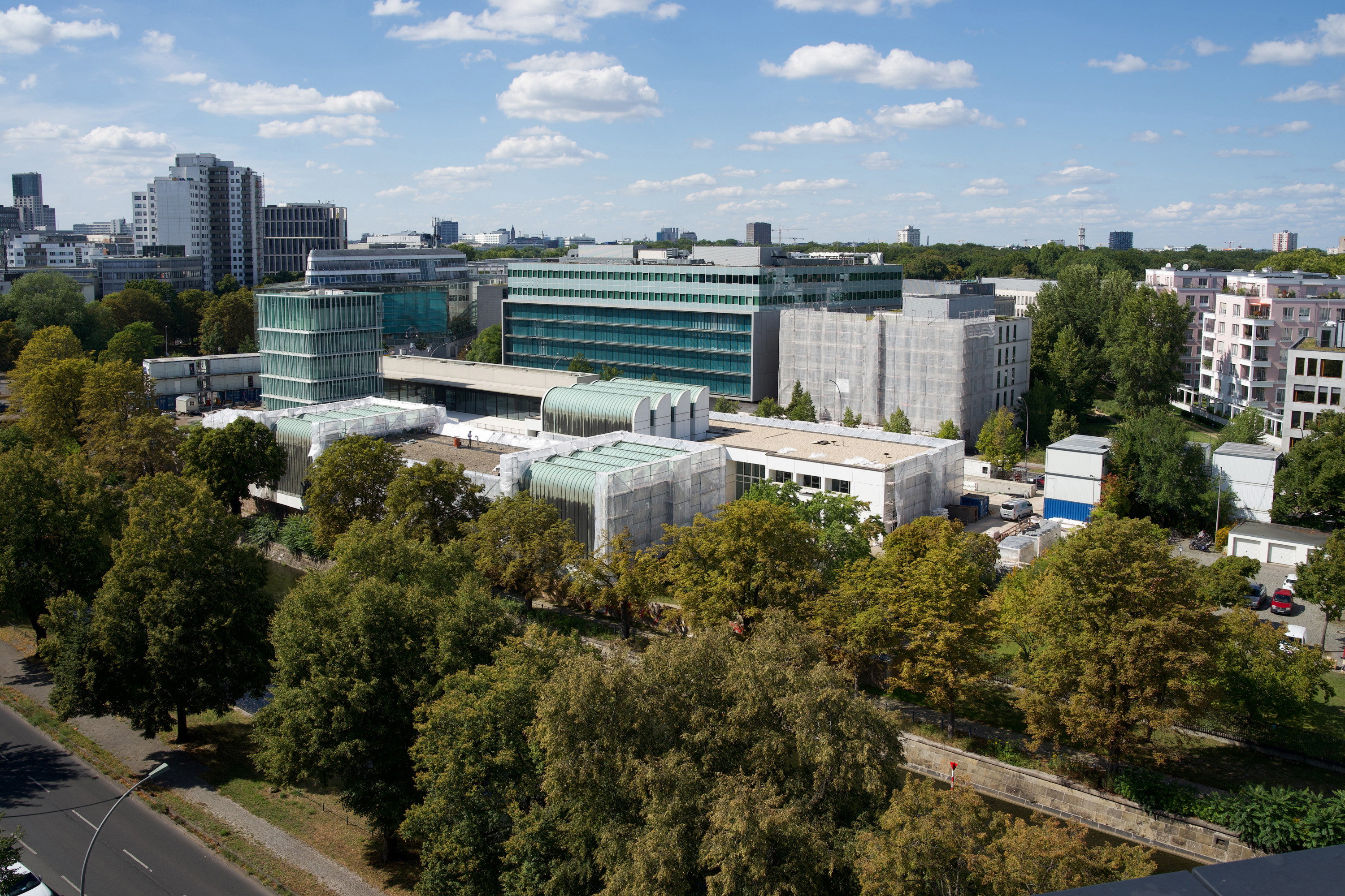Luftaufnahme moderner Gebäude inmitten von Grün unter blauem Himmel mit Wolken, die städtische Architektur zeigt.