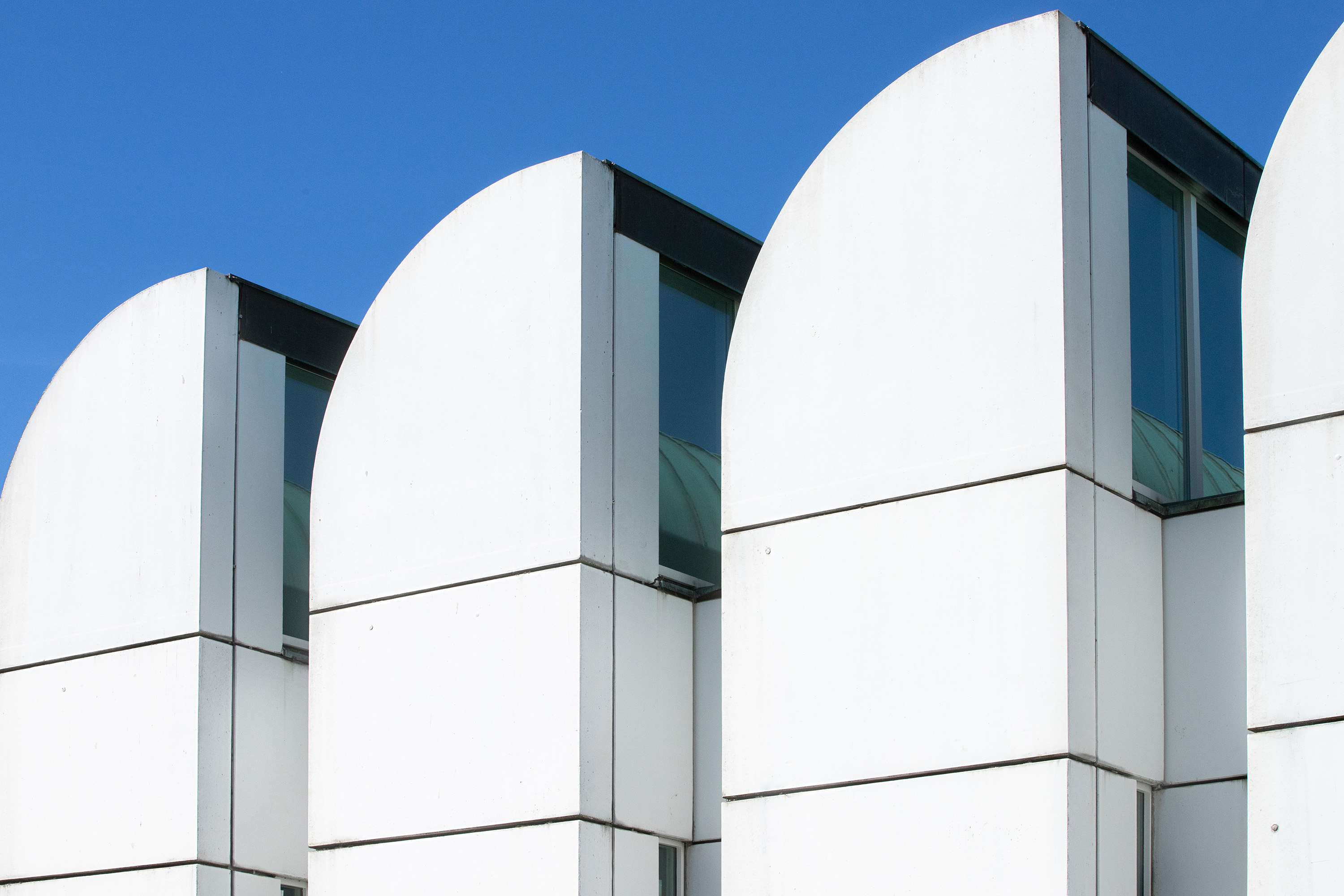 Moderne Architektur mit leicht gewölbten Dächern und großen Fenstern, vor blauem Himmel.