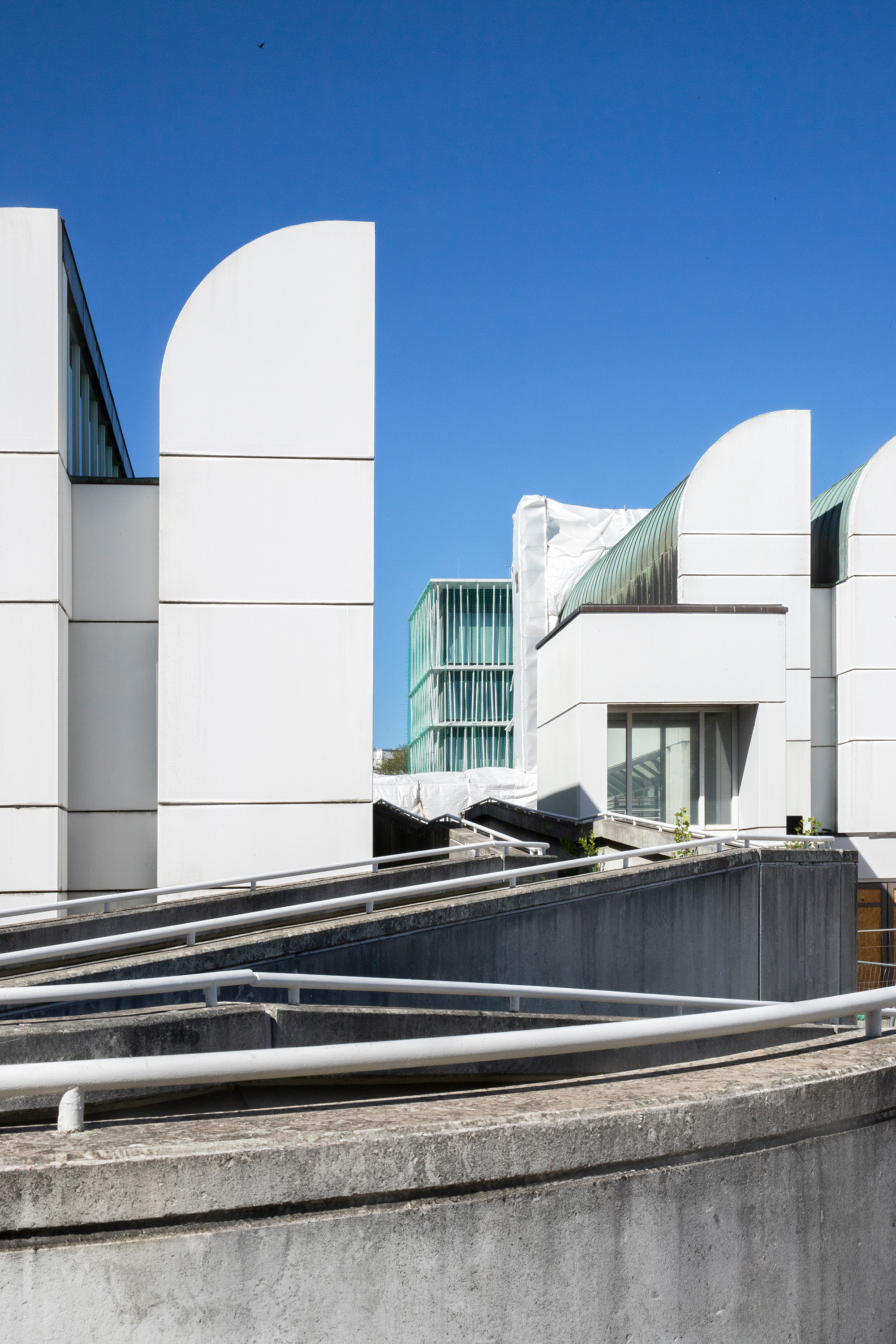 Moderne Architektur mit weißen Wänden und einem klaren blauen Himmel im Hintergrund. Geometrische Formen dominieren die Szene.