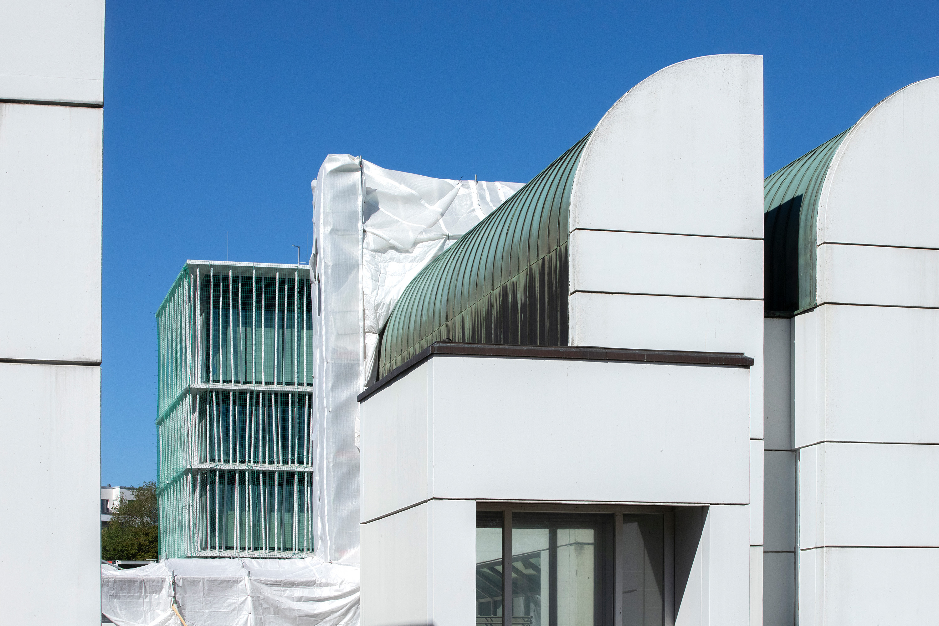 Moderne Architektur mit weißen Fassaden und charakteristischen Dächern, im Hintergrund ein weiteres Gebäude in Bau.