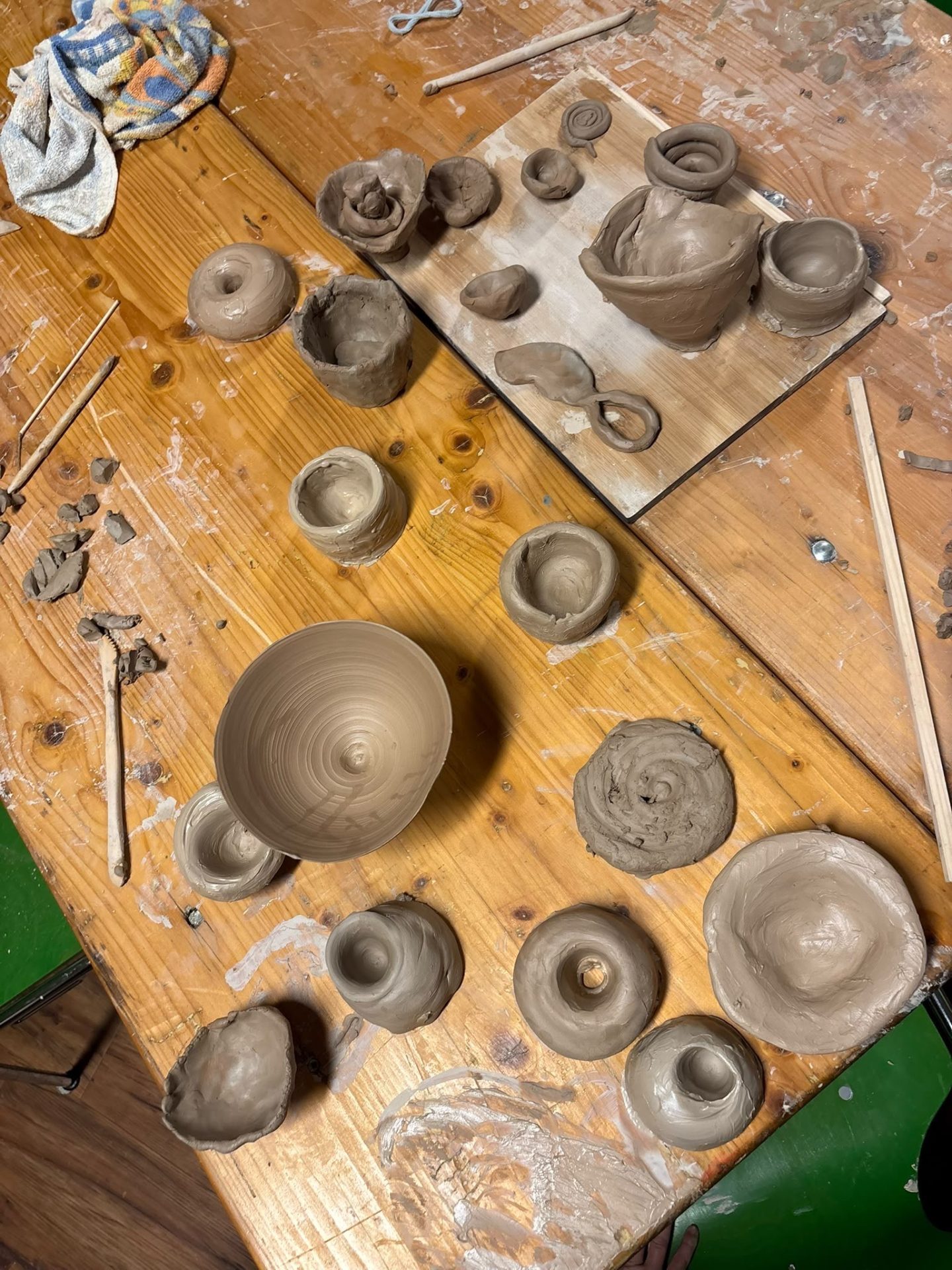 Clay pots and kitchen utensils on a wooden table, surrounded by tools and a cloth.